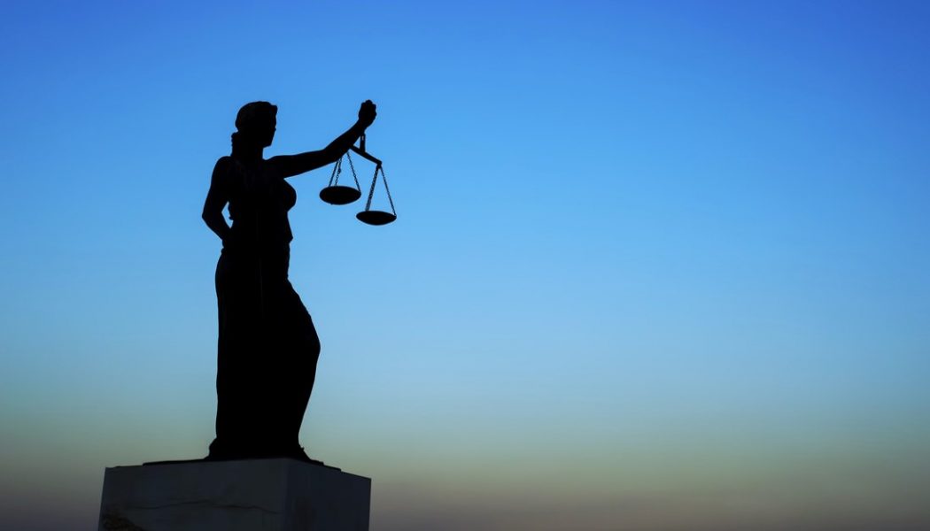 Blindfolded Lady Justice holding scales silhouetted against a dark sky